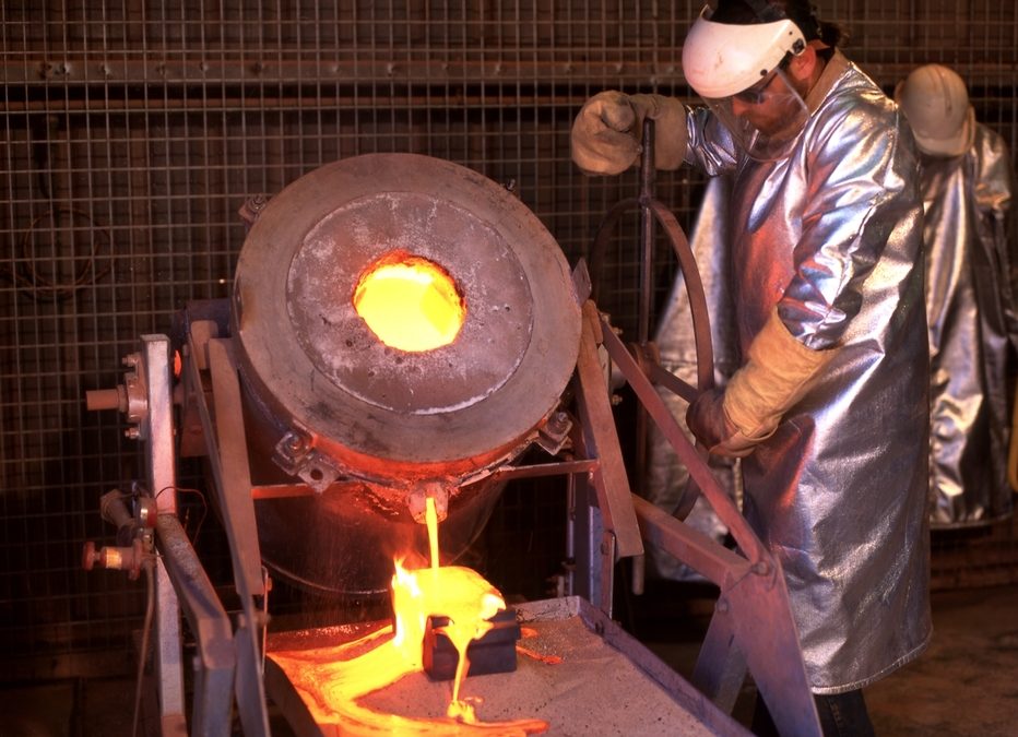 View of gold mine worker wearing heat protective clothing pouring molten gold into an ingot mold (NT)